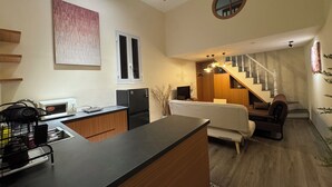 Une cuisine moderne avec un îlot central, un coin repas comprenant un canapé et des chaises, un escalier menant à un étage supérieur et un petit miroir rond accroché au mur.