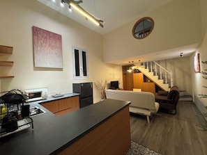 Eine moderne Küche mit Kochinsel, einem Essbereich mit Sofa und Sesseln, einer Treppe zu einer oberen Ebene und einem kleinen runden Spiegel an der Wand.