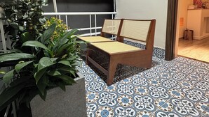 Un balcon avec une chaise en bois, un pot de fleurs et des carreaux de sol à motifs.