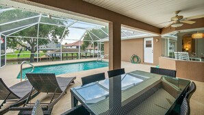 Ein überdachter Poolbereich mit Glastisch und -stühlen, Deckenventilator und Blick auf die umliegende Landschaft.