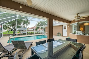 Ein überdachter Poolbereich mit Glastisch und -stühlen, Deckenventilator und Blick auf die umliegende Landschaft.