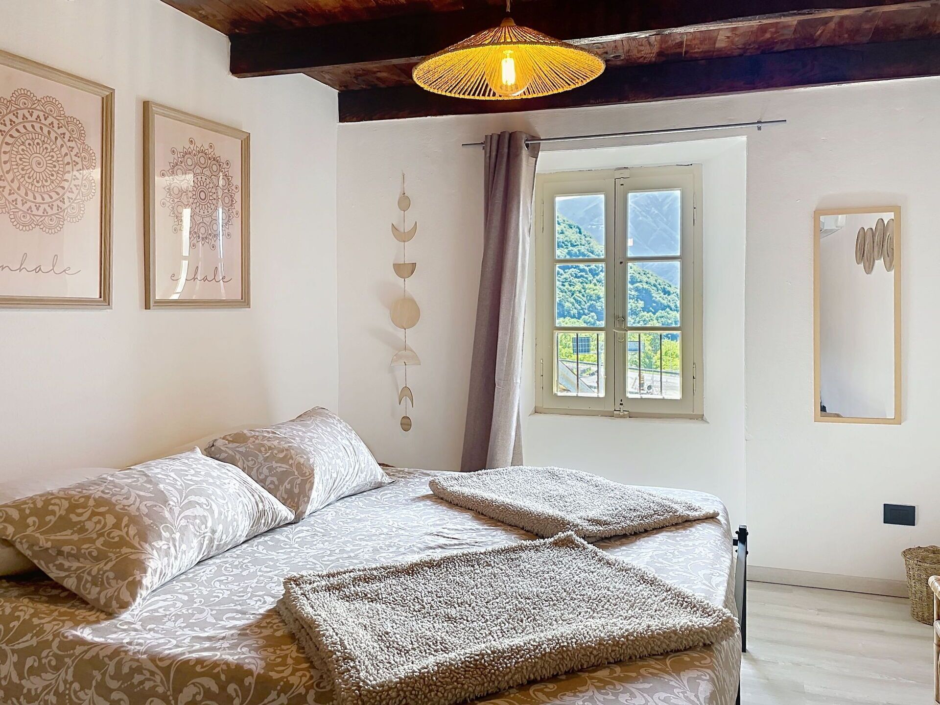 Une chambre à coucher avec un lit, un luminaire suspendu, une fenêtre donnant sur un paysage agréable et des œuvres d’art murales.