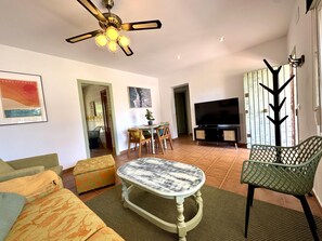 Uma sala de estar com ventilador de teto, televisão, mesa de jantar com cadeiras e um sofá.