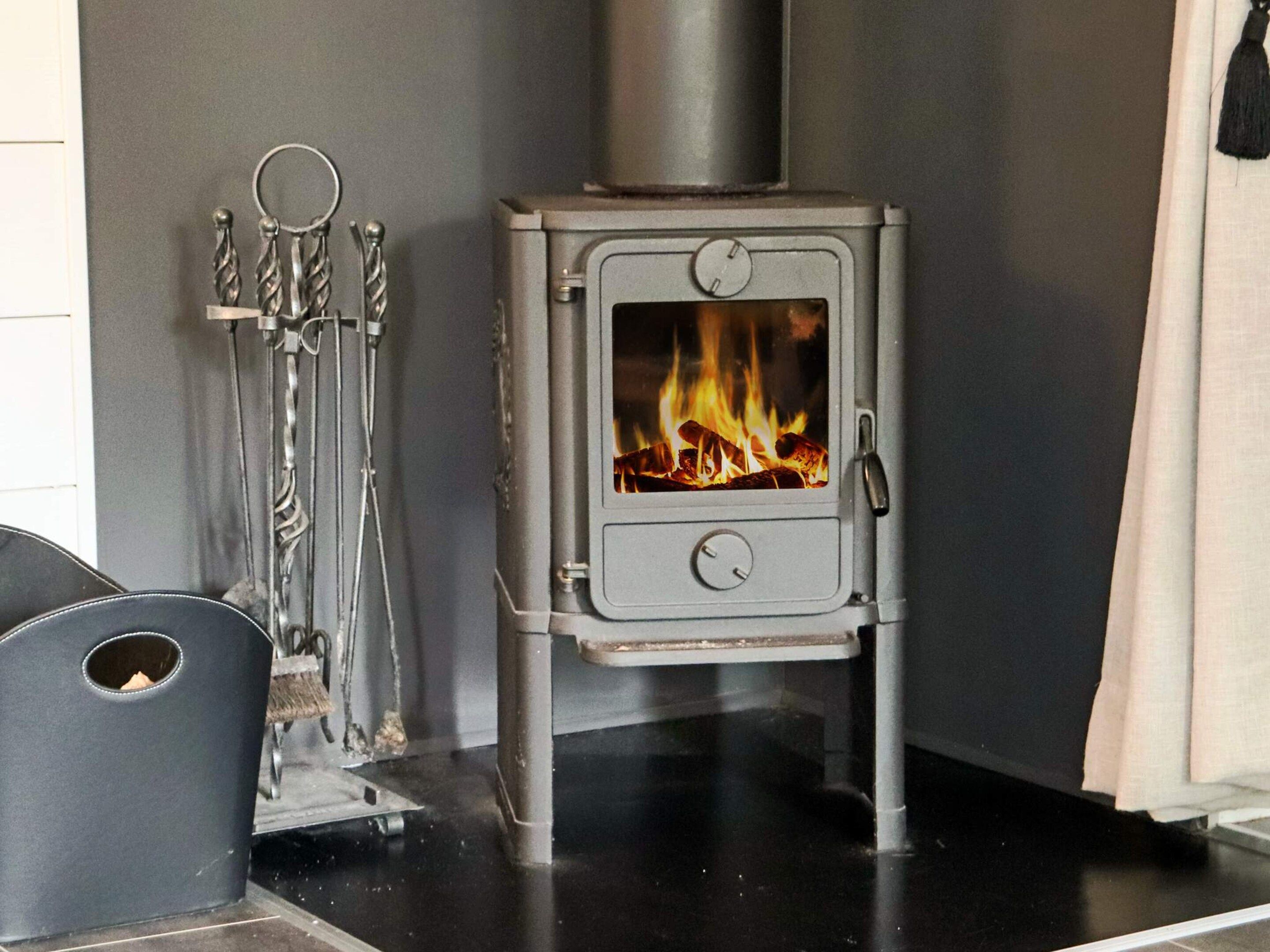 A wood-burning stove with a visible fire, a metal tool rack, and a black metal bench.