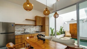 A modern kitchen with wooden cabinets, a marble countertop, and a dining area with a wooden table and chairs. - Family 2 Bedroom Villa by Seminyak - B13 (Kota Denpasar)