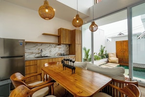 A modern kitchen with wooden cabinets, a marble countertop, and a dining area with a wooden table and chairs. - Family 2 Bedroom Villa by Seminyak - B13 (Kota Denpasar)