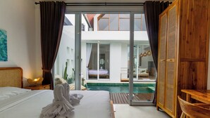 A hotel room with a bed, a wooden wardrobe, a glass door leading to a pool area, and a view of the outside. - Family 2 Bedroom Villa by Seminyak - B13 (Kota Denpasar)