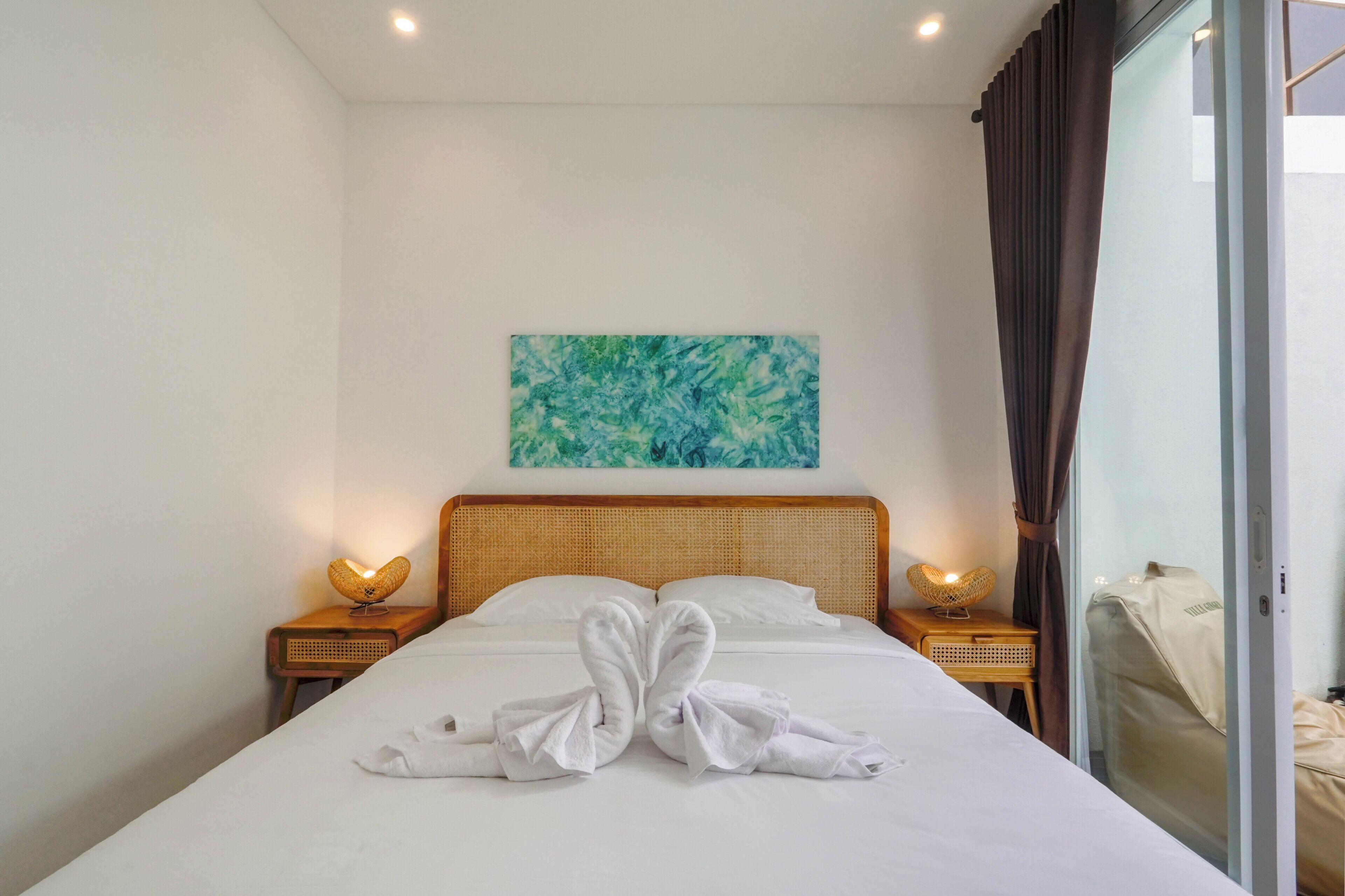 A hotel room with a bed, two bedside lamps, a painting on the wall, and a window with curtains.