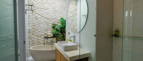 Un bagno con parete in pietra, una vasca da bagno indipendente, uno specchio e un lavabo con mobile in legno.