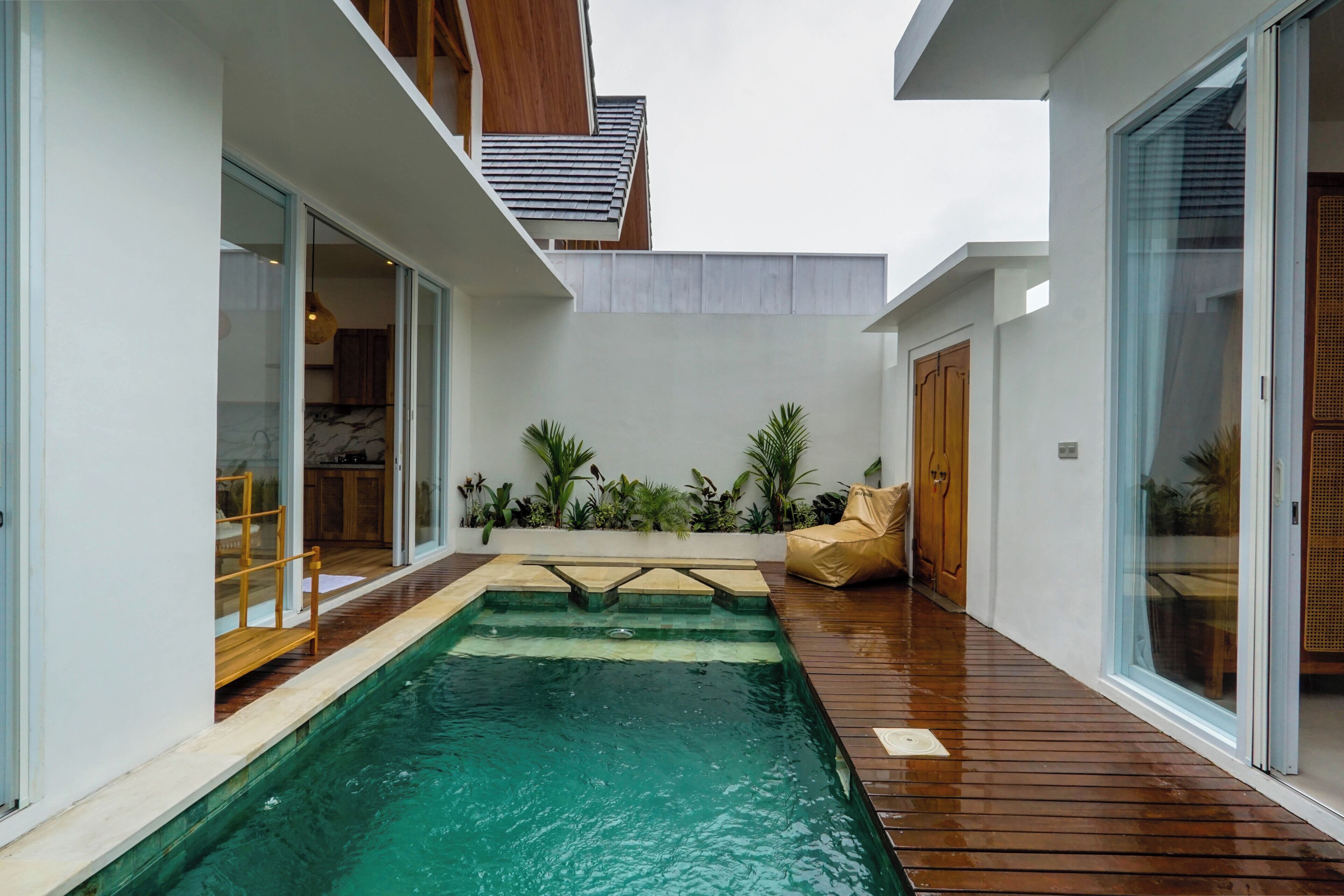 A modern outdoor pool area with a wooden deck, glass doors, and potted plants.