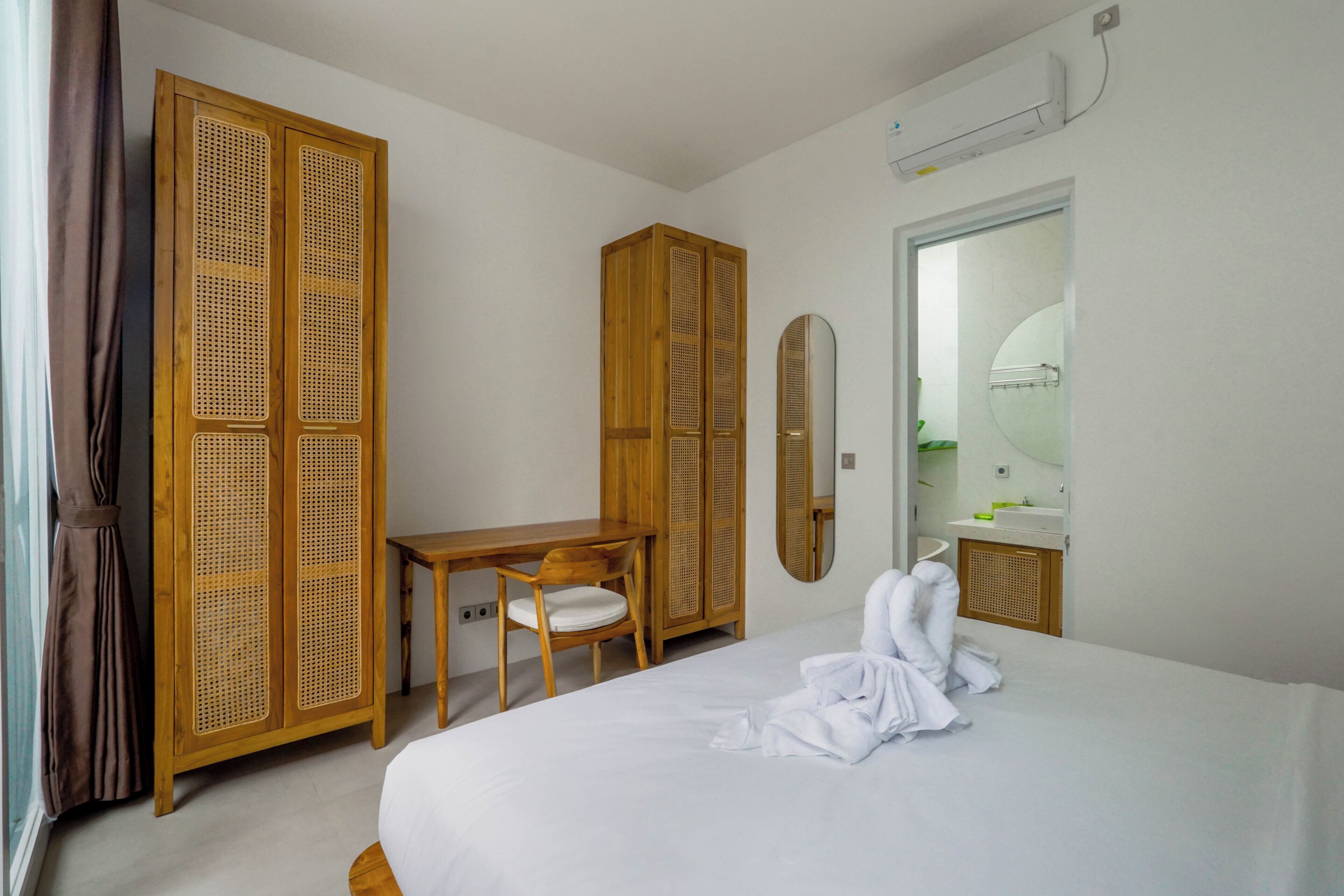 A hotel room with a bed, a wooden wardrobe, a desk, a chair, and a mirror.