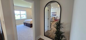 Un couloir avec un grand miroir qui reflète une chambre à coucher, un coin repas et une vue sur l’extérieur.