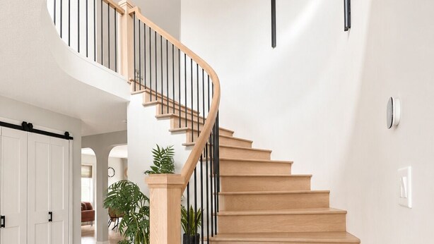 A spiral staircase with wooden steps and black railings, leading to a landing with a potted plant.