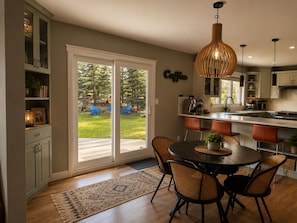 A modern kitchen with a dining area, large windows, and a view of the backyard.