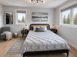 A bedroom with a bed, bedside tables, a chair, a rug, a mirror, and a painting.