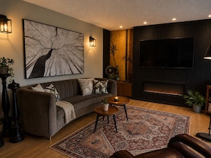A modern living room with a sofa, a coffee table, a fireplace, a large TV, and a decorative wall piece.