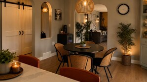 A dining area with a round table, wicker chairs, a hanging light fixture, and a wall clock.