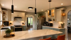 A modern kitchen with a central island, stainless steel appliances, pendant lighting, and a view to a dining area.