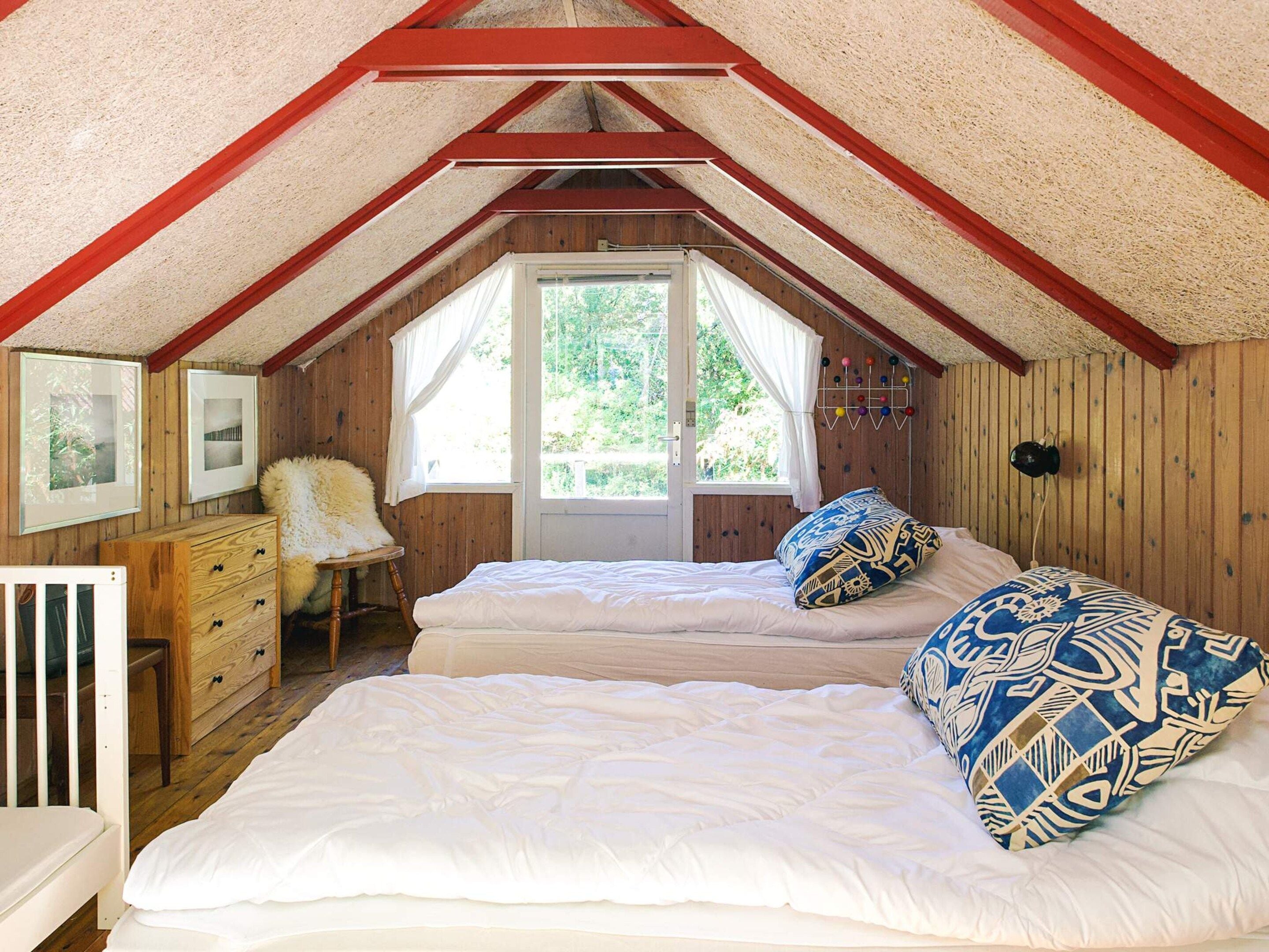 Un dormitorio acogedor en el ático, con dos camas, paredes de madera, una ventana y un aparador.