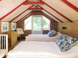 A cozy attic bedroom with two beds, wooden walls, a window, and a dresser. - 4 Star Holiday Home in Sejero (Sejero)