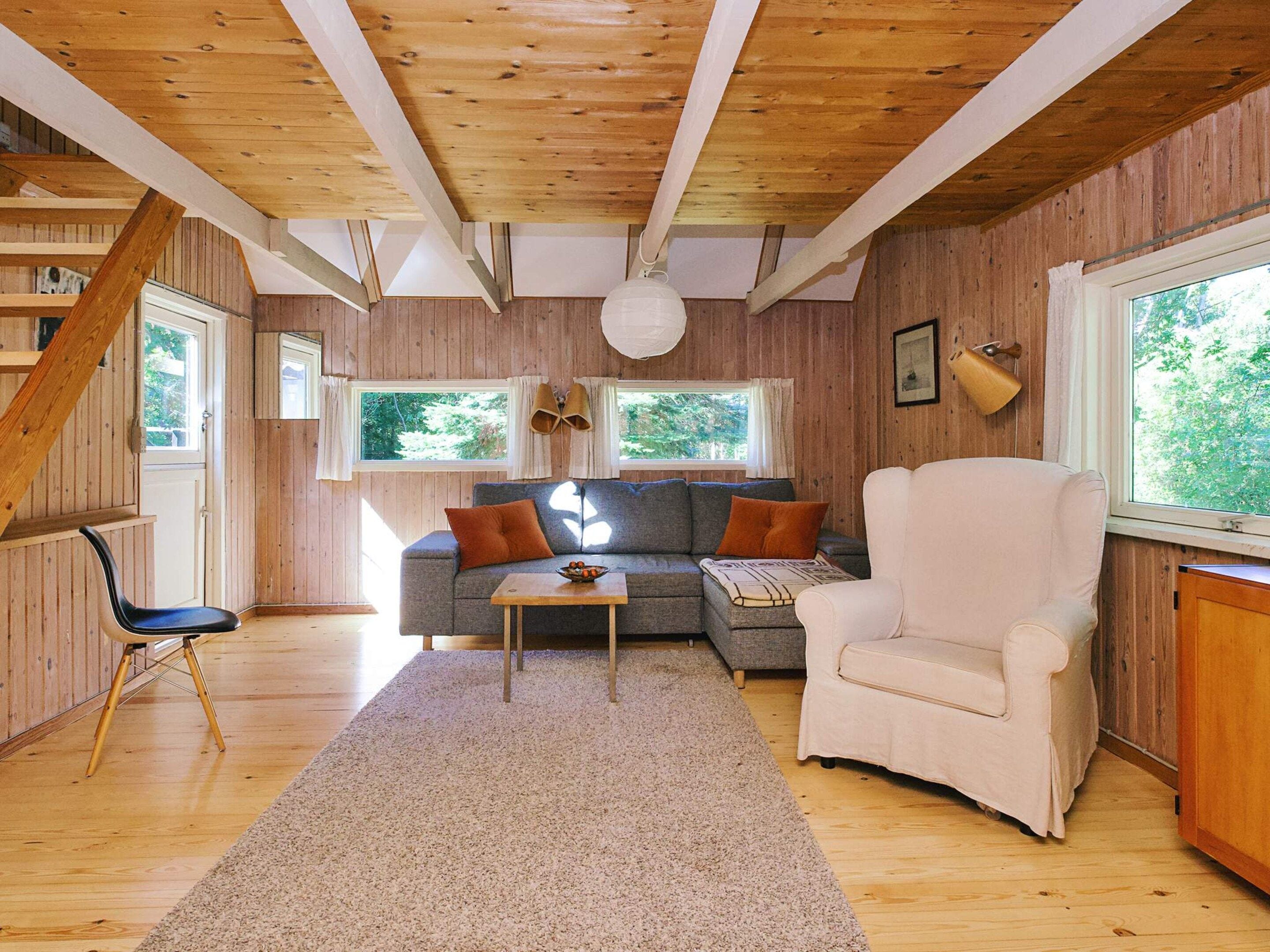 Una sala acogedora con sofá, sillón y una mesita. Hay una ventana con cortinas y vistas a zonas verdes.