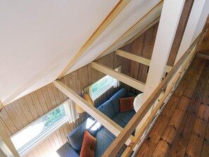 Una habitación tipo loft con techo inclinado, vigas de madera, un sofá azul y una ventana.