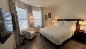 A hotel room with a bed, a chair, a side table, a lamp, and a TV.
