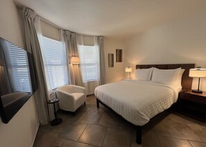 Ein Hotelzimmer mit Bett, Sessel, Nachttisch, Lampe und Fernseher.