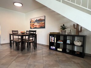 A dining area with a table and chairs, a bookshelf with books and decorative items, and a painting on the wall. - Arrowzona Mountain Home - Phoenix (Phoenix)