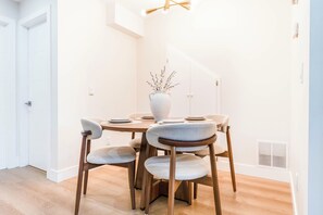 Ein Essbereich mit einem runden Tisch, sechs Stühlen, einer Vase mit Ästen und einer Deckenleuchte.