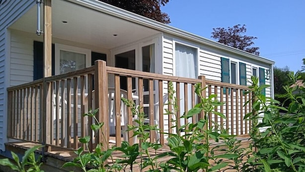 Une maison de plain-pied dotée d’une terrasse en bois, d’un porche couvert et d’une fenêtre avec des volets verts.