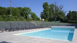 Une piscine avec des chaises longues, un espace délimité par une clôture et des arbres en arrière-plan.