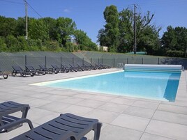 Une piscine avec des chaises longues, un espace délimité par une clôture et des arbres en arrière-plan.