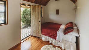 Een slaapkamer met een houten plafond, een bed met rode beddengoed, een wit tapijt en een deur naar een buitenruimte.