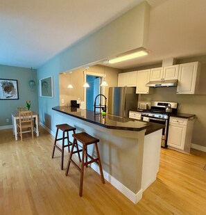 Una cocina moderna con una isla central, taburetes de bar, refrigerador, estufa, microondas y armarios blancos.