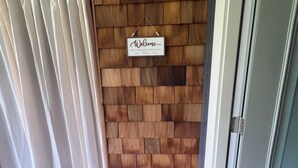 Un mur en bois avec une pancarte de bienvenue, une porte et un paillasson noir sur un plancher en bois.