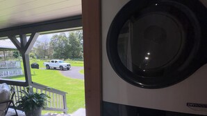 Une buanderie équipée de deux machines à laver et deux sèche-linge superposés, une terrasse en bois et une vue sur l’allée et la pelouse.