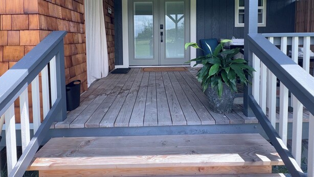Une terrasse en bois avec une rambarde, un pot de fleurs et une porte à panneaux de verre.