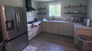 Une cuisine moderne équipée d’un réfrigérateur en acier inoxydable, d’une cuisinière à gaz, de meubles en bois, d’une fenêtre et d’une poubelle.