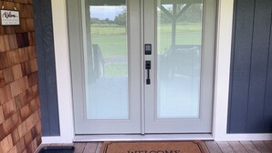 Une porte d’entrée à deux battants, agrémentée d’un paillasson sur lequel est écrit « Bienvenue », d’une serrure à clavier et d’un mur en bois sur lequel est affiché un panneau « Bienvenue ».