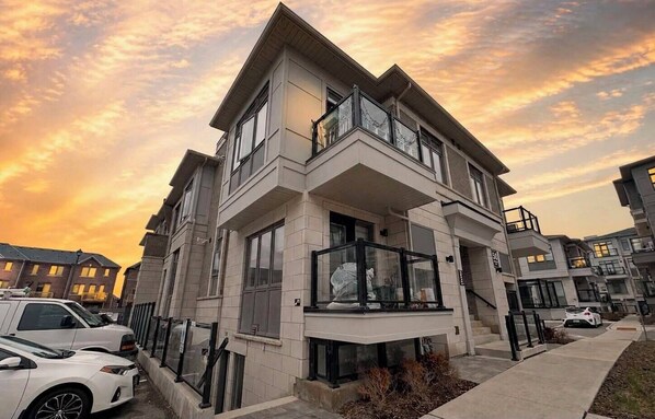 A multi-story residential building with balconies, a driveway, and parked cars.