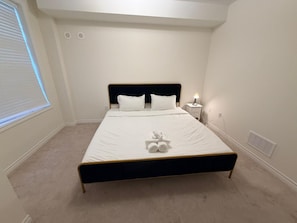 Una cama bien hecha con sábanas blancas, una lámpara de noche y un osito de peluche sobre la cama.