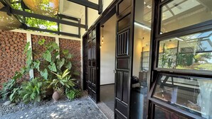 Ingresso di un edificio moderno con parete in mattoni, grandi piante in vaso e porta in vetro.