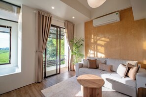 Ein modernes Wohnzimmer mit einer Couch, einem runden Holztisch und einem großen Fenster mit Vorhängen.