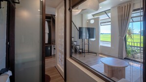 Una camera d'albergo moderna con un'ampia finestra, un pavimento in legno, un tavolo rotondo e una scala che conduce a un piano superiore.