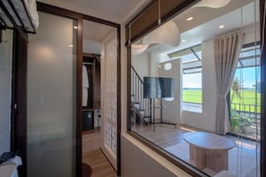 Ein modernes Hotelzimmer mit großem Fenster, Holzboden, rundem Tisch und einer Treppe, die zu einer oberen Ebene führt.