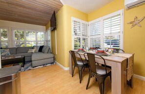 A living room with a sofa, dining table, chairs, and a kitchen area with a stove. - Pacific Beach Family Escape/Hot tub+Lg Play Yard (San Diego)