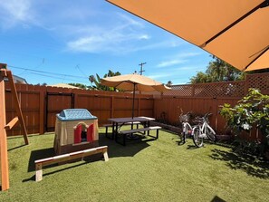 A backyard with artificial grass, a playhouse, a picnic table, a bicycle, and a wooden fence. - Pacific Beach Family Escape/Hot tub+Lg Play Yard (San Diego)