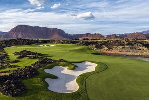 Ein Golfplatz mit Bunkern, einem Wasserhindernis und Bergen im Hintergrund.