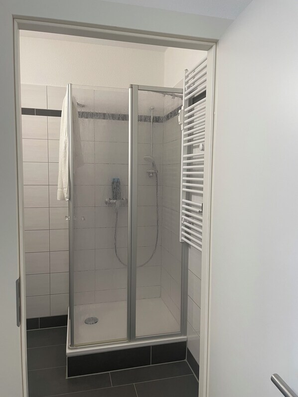 Une cabine de douche fermée par des parois en verre, avec une serviette blanche accrochée à la porte.